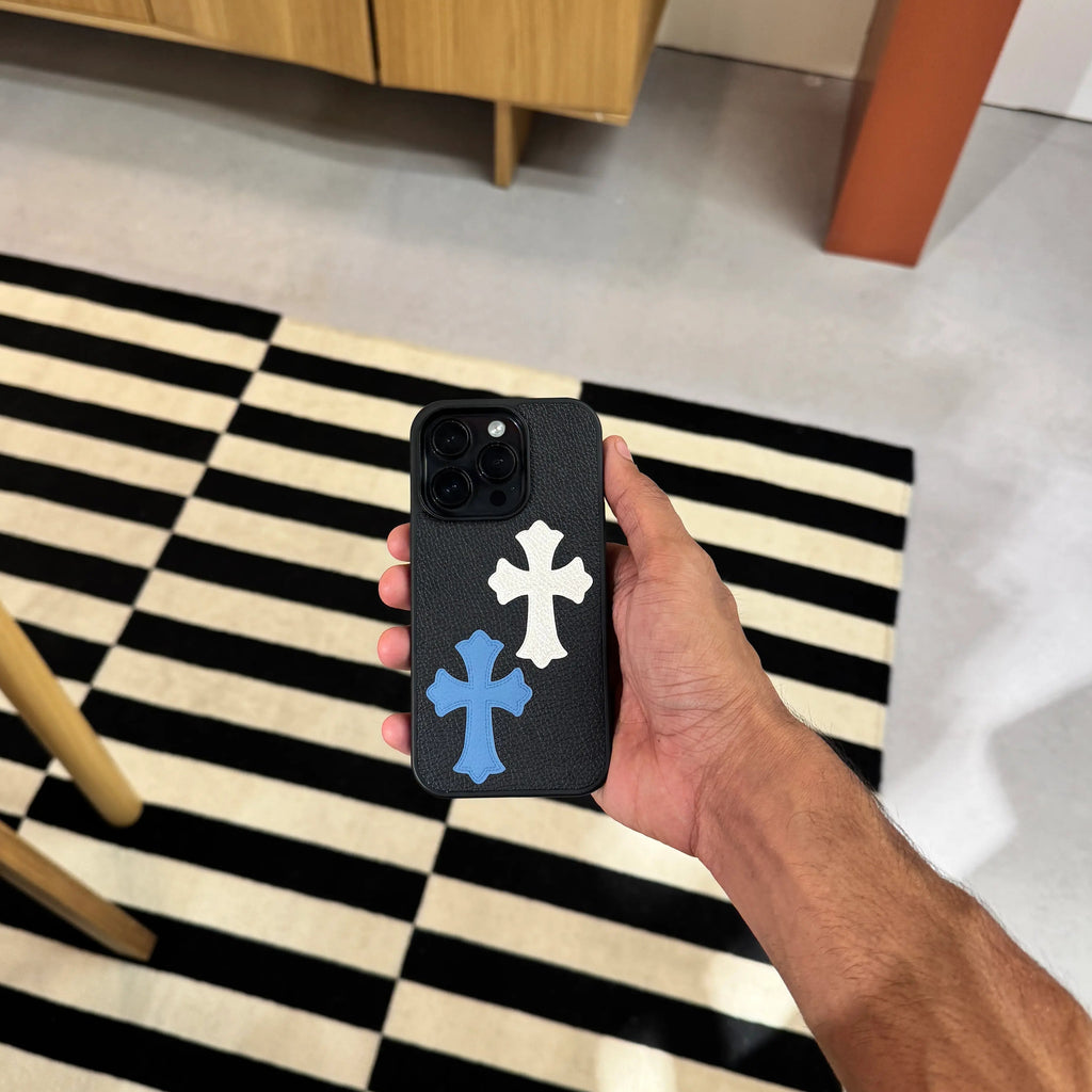 Person holding a phone with a case featuring two crosses on a black and white striped rug.